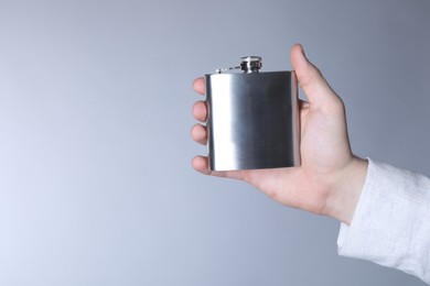 Man holding metal hip flask on light grey background, closeup. Space for text