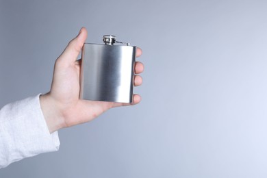 Man holding metal hip flask on light grey background, closeup. Space for text