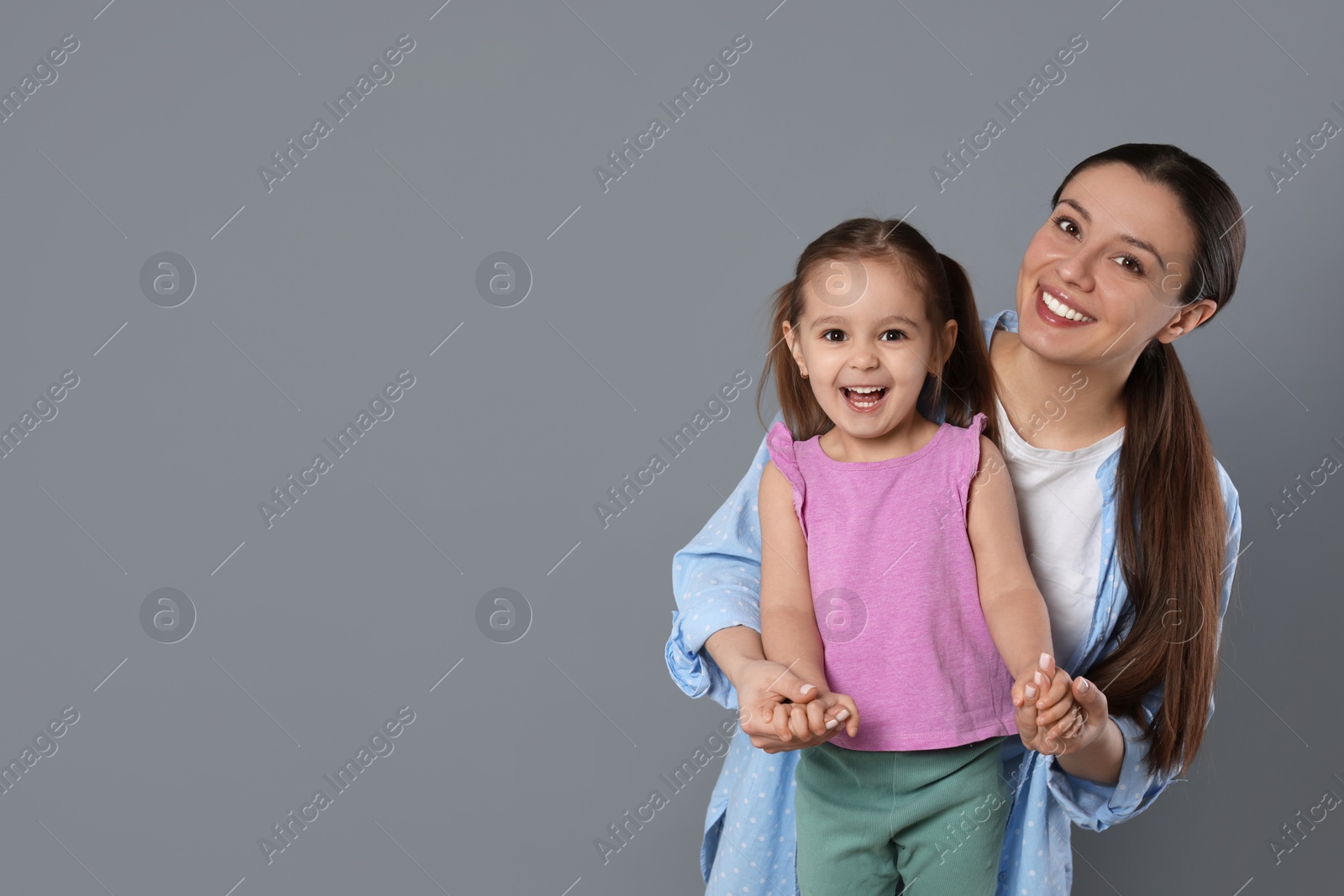 Photo of Portrait of happy mother and her cute little daughter on grey background, space for text