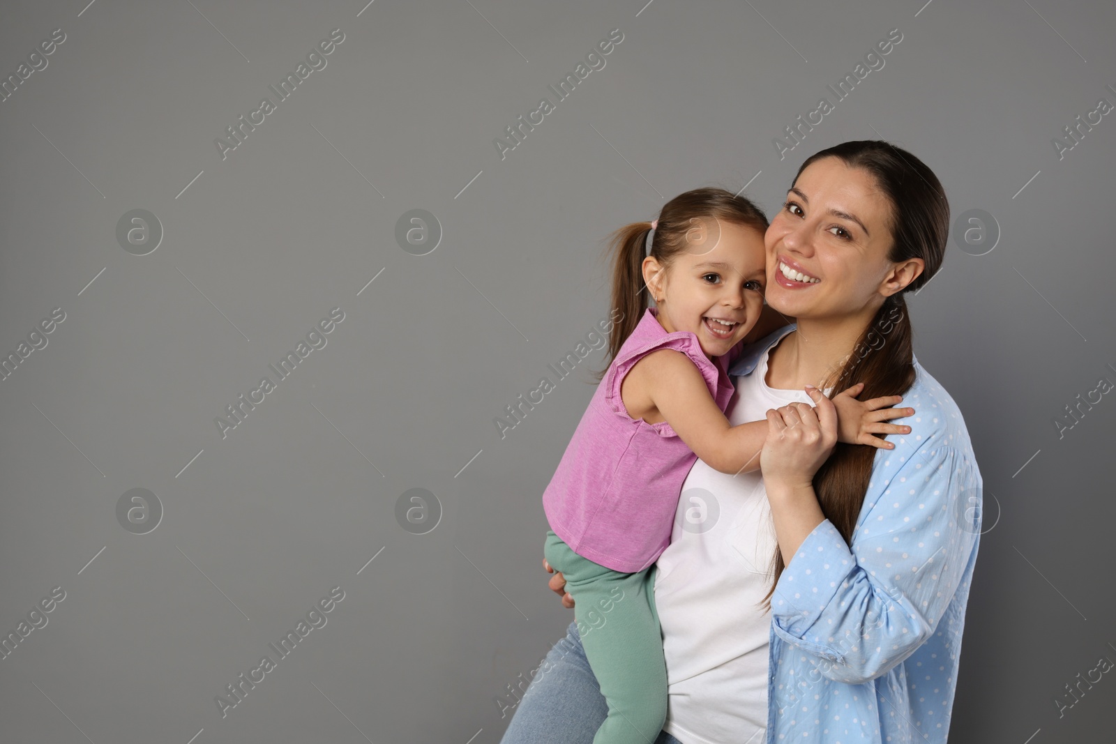 Photo of Portrait of happy mother and her cute little daughter on grey background, space for text