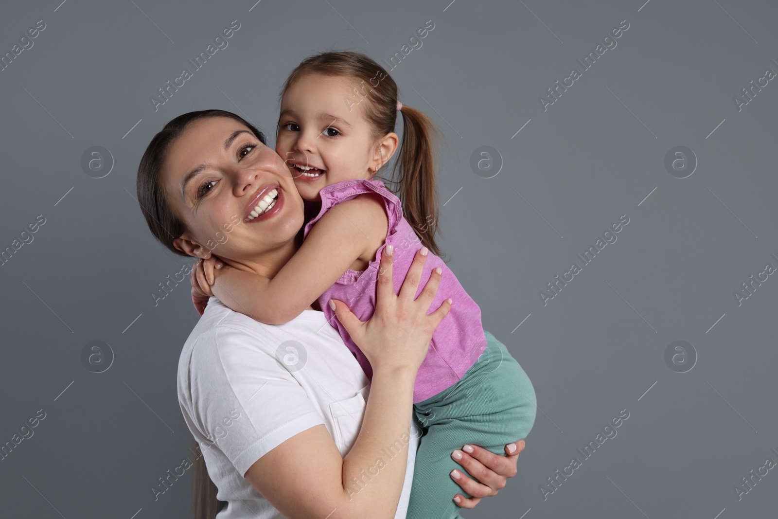 Photo of Portrait of happy mother and her cute little daughter on grey background, space for text