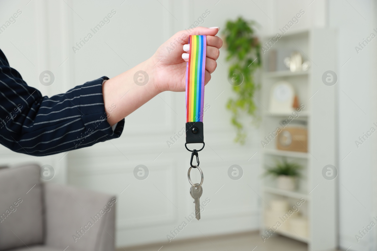 Photo of Woman holding key with keychain in LGBT colors indoors, closeup