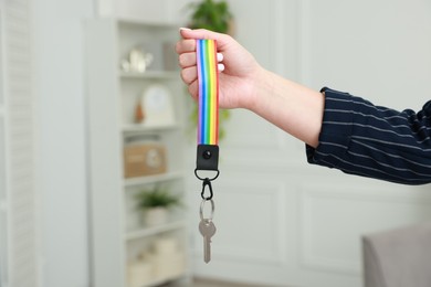 Photo of Woman holding key with keychain in LGBT colors indoors, closeup