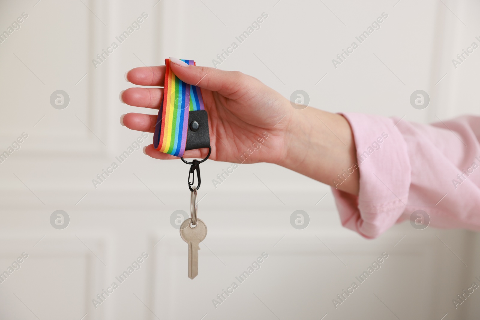 Photo of Woman holding key with keychain in LGBT colors indoors, closeup