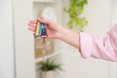 Photo of Woman holding key with keychain in LGBT colors indoors, closeup