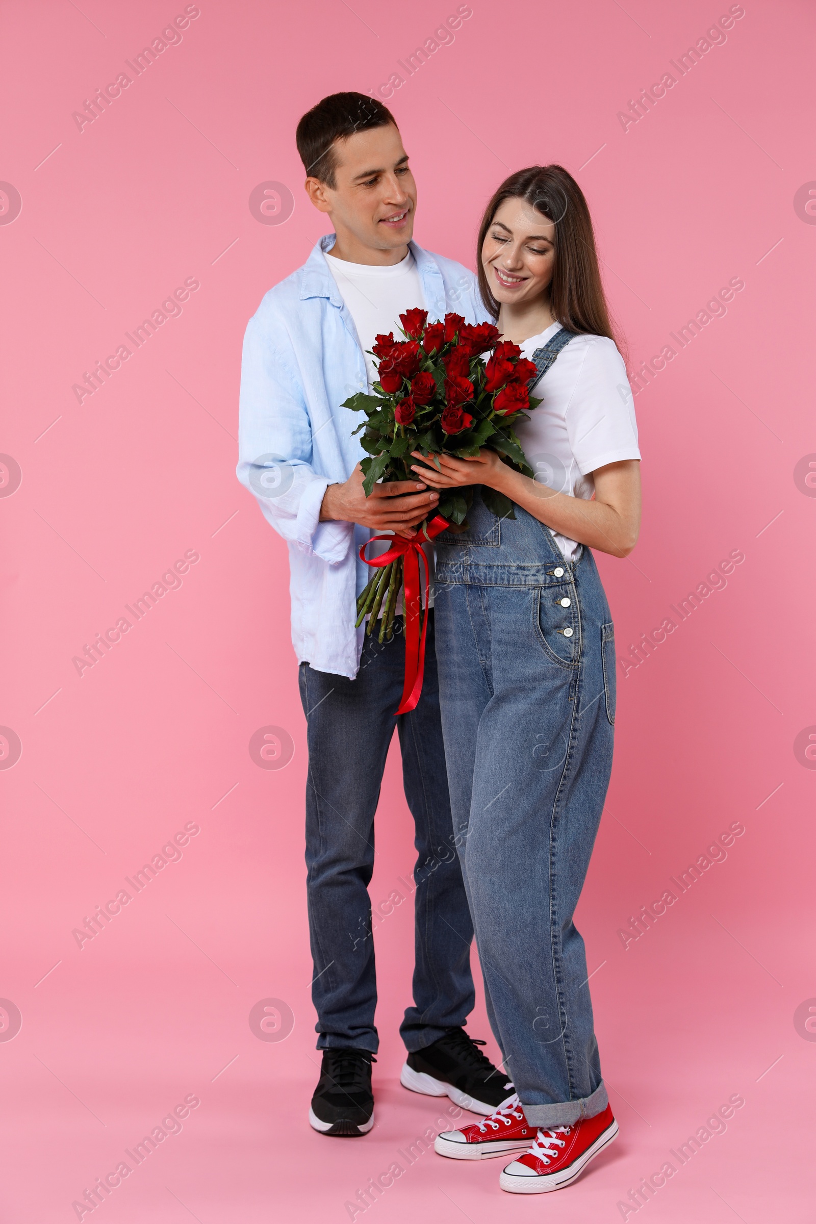 Photo of Lovely couple with bouquet of red roses on pink background. Valentine's day celebration