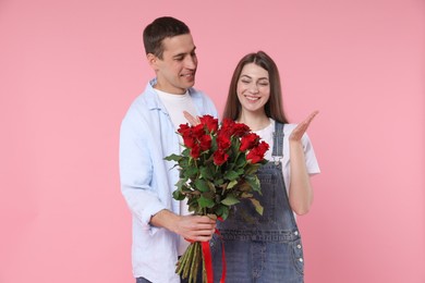 Photo of Lovely couple with bouquet of red roses on pink background. Valentine's day celebration