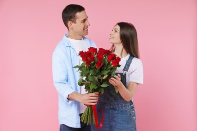 Photo of Lovely couple with bouquet of red roses on pink background. Valentine's day celebration