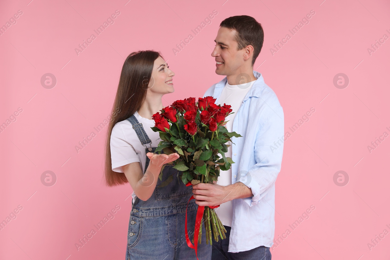 Photo of Lovely couple with bouquet of red roses on pink background. Valentine's day celebration