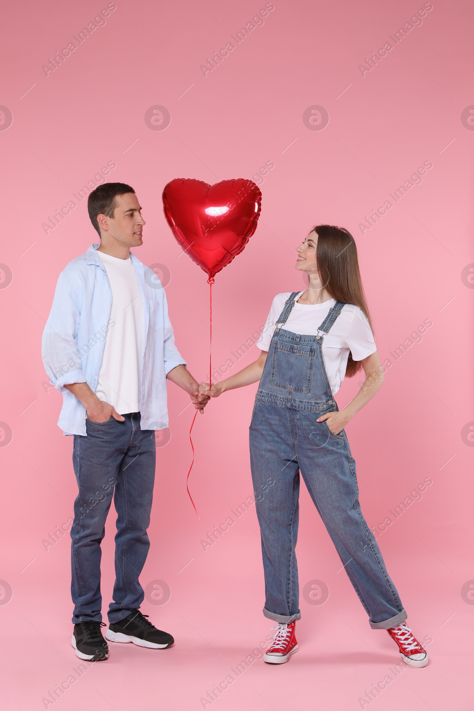 Photo of Lovely couple with heart shaped balloon on pink background. Valentine's day celebration