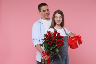 Photo of Lovely couple with bouquet of red roses and gift box on pink background. Valentine's day celebration