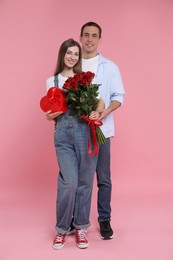 Photo of Lovely couple with bouquet of red roses and gift box on pink background. Valentine's day celebration