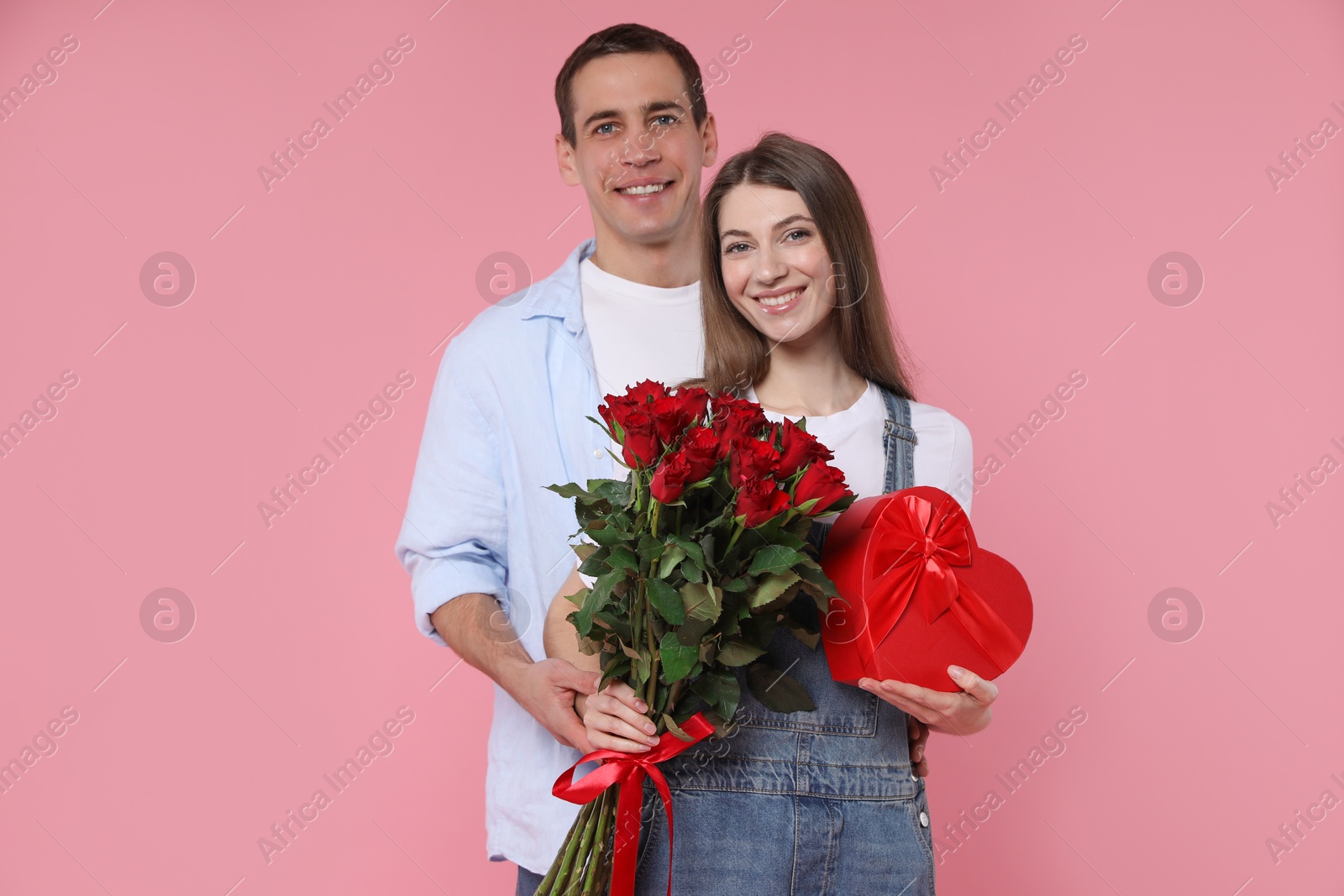 Photo of Lovely couple with bouquet of red roses and gift box on pink background. Valentine's day celebration