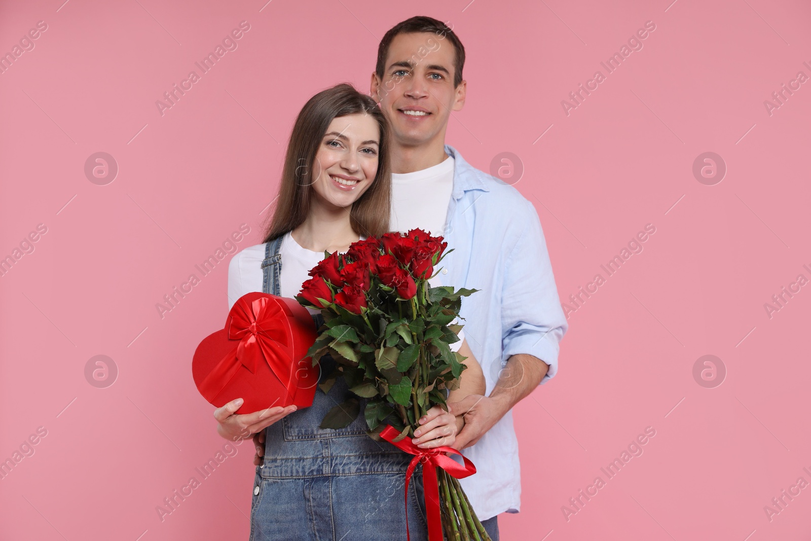 Photo of Lovely couple with bouquet of red roses and gift box on pink background. Valentine's day celebration