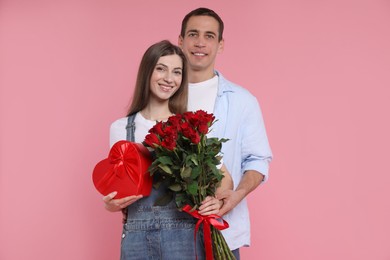 Photo of Lovely couple with bouquet of red roses and gift box on pink background. Valentine's day celebration