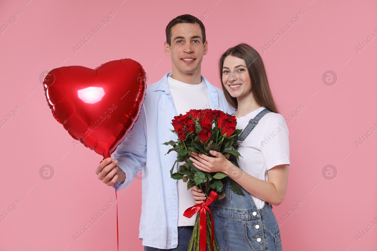 Photo of Lovely couple with bouquet of red roses and heart shaped balloon on pink background. Valentine's day celebration