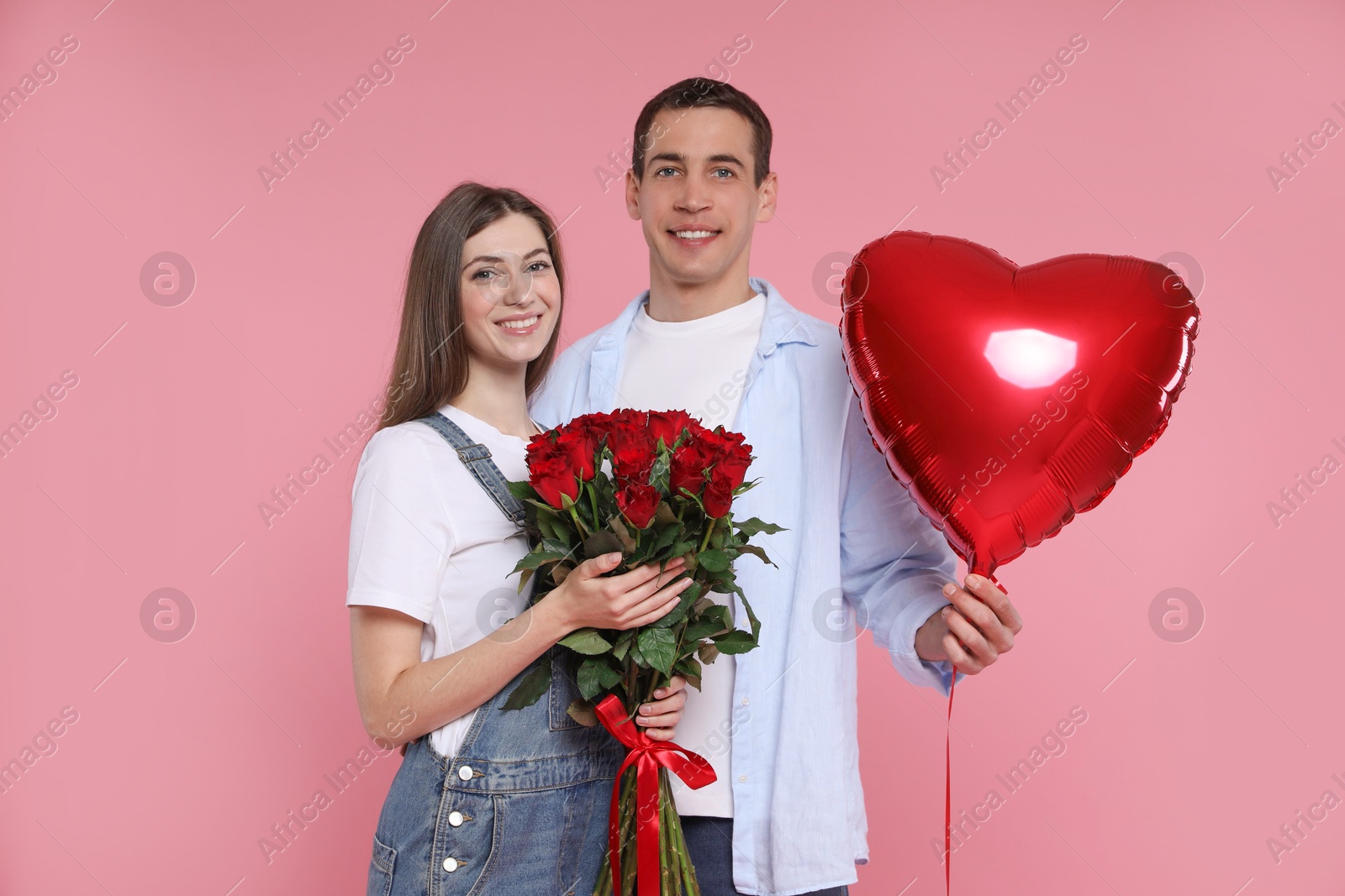 Photo of Lovely couple with bouquet of red roses and heart shaped balloon on pink background. Valentine's day celebration