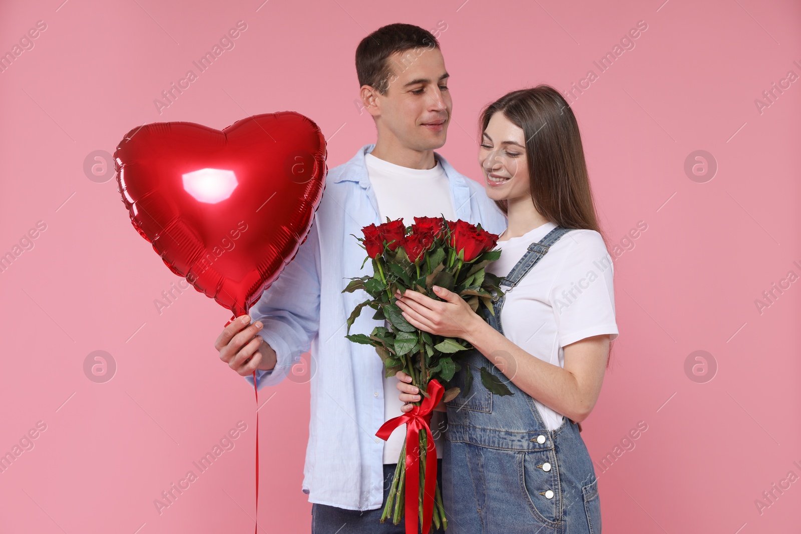 Photo of Lovely couple with bouquet of red roses and heart shaped balloon on pink background. Valentine's day celebration