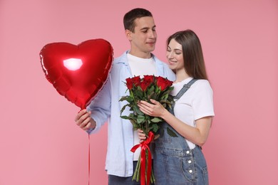 Photo of Lovely couple with bouquet of red roses and heart shaped balloon on pink background. Valentine's day celebration