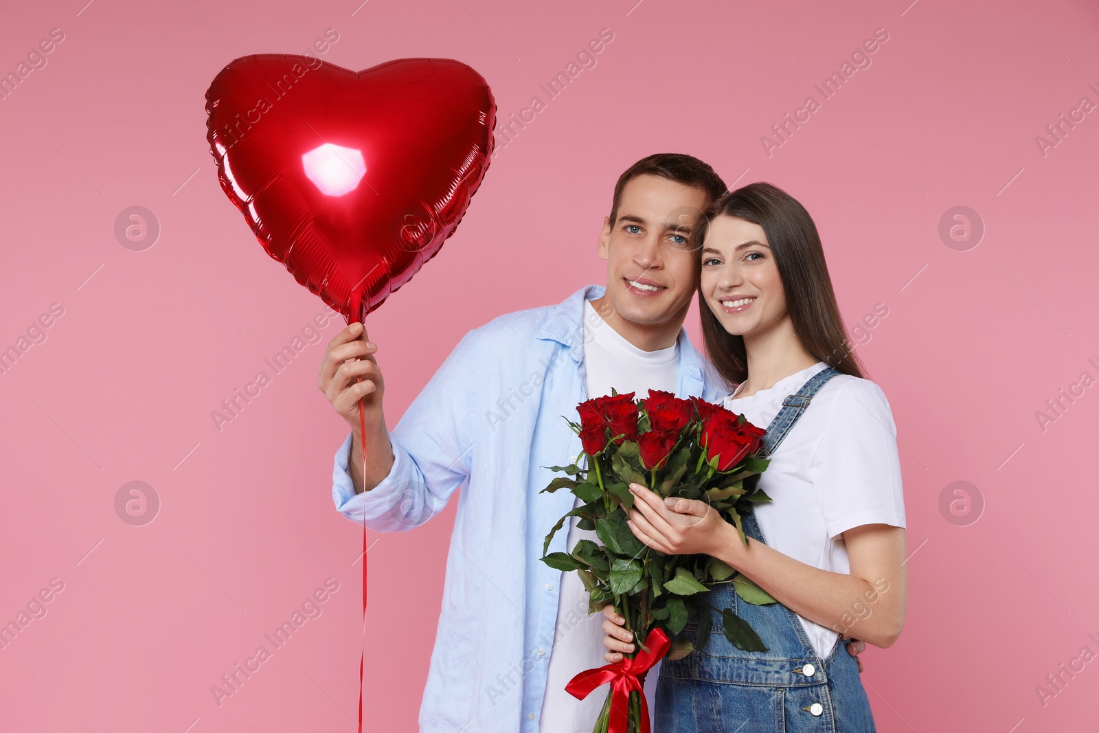 Photo of Lovely couple with bouquet of red roses and heart shaped balloon on pink background. Valentine's day celebration