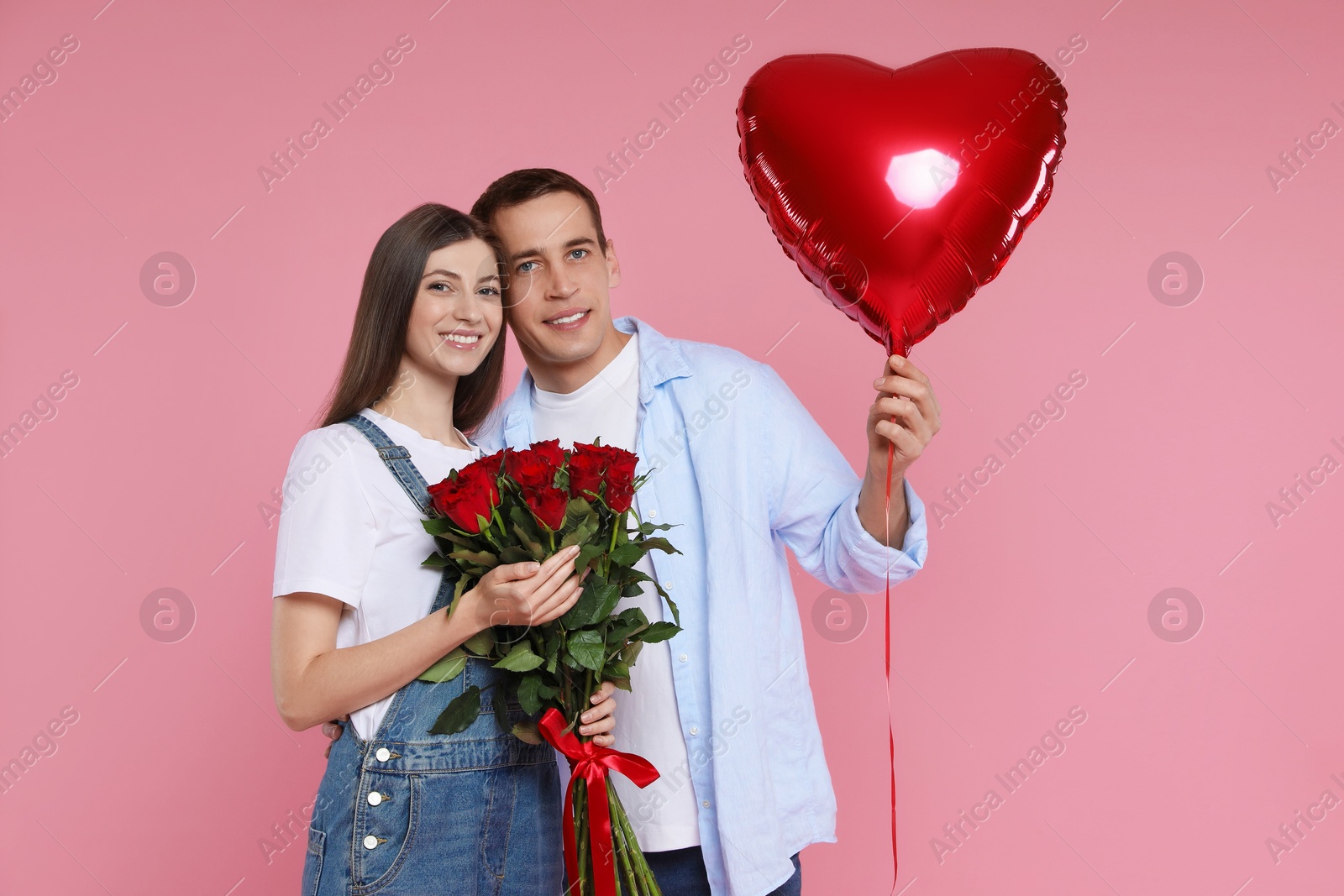 Photo of Lovely couple with bouquet of red roses and heart shaped balloon on pink background. Valentine's day celebration