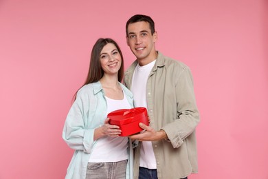 Photo of Lovely couple with gift box on pink background. Valentine's day celebration