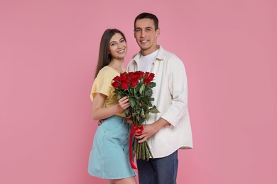 Photo of Lovely couple with bouquet of red roses on pink background. Valentine's day celebration