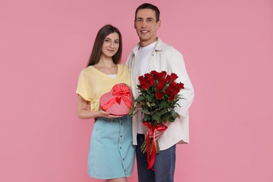 Photo of Lovely couple with bouquet of red roses and gift box on pink background. Valentine's day celebration