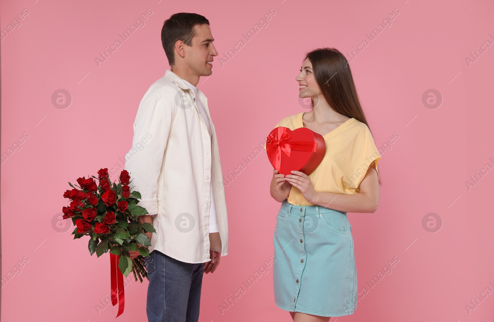 Photo of Lovely couple with bouquet of red roses and gift box on pink background. Valentine's day celebration