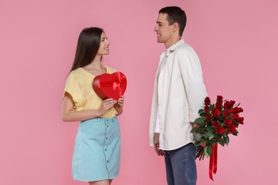 Photo of Lovely couple with bouquet of red roses and gift box on pink background. Valentine's day celebration