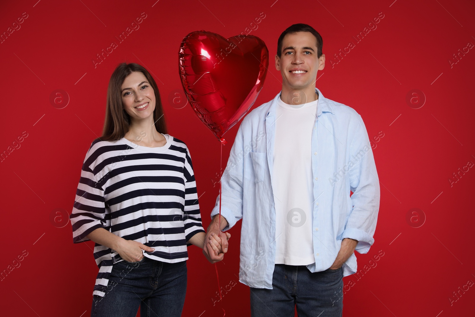 Photo of Lovely couple with heart shaped balloon on red background. Valentine's day celebration