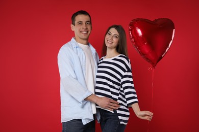 Photo of Lovely couple with heart shaped balloon on red background. Valentine's day celebration