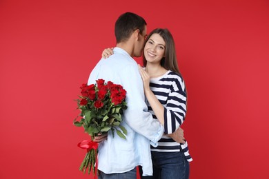 Photo of Lovely man hiding bouquet of roses for his beloved woman on red background. Valentine's day celebration