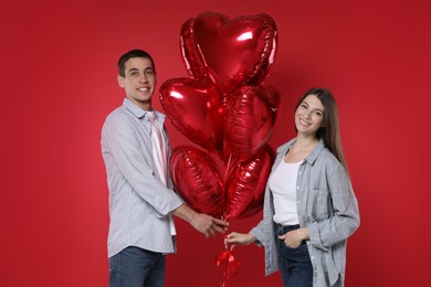 Photo of Lovely couple with heart shaped balloons on red background. Valentine's day celebration