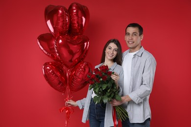 Photo of Lovely couple with heart shaped balloons and bouquet of roses on red background. Valentine's day celebration