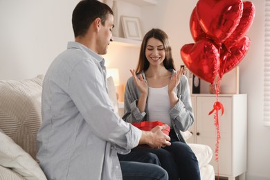 Photo of Lovely man surprising his girlfriend with Valentine's day gift indoors