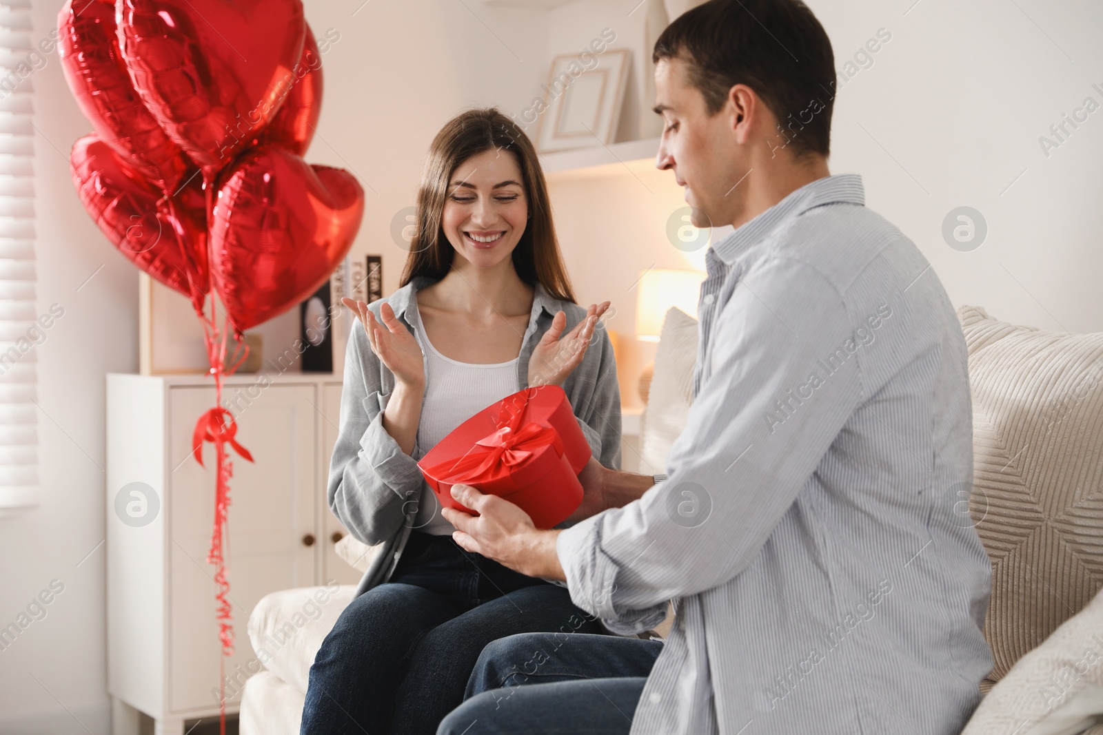 Photo of Lovely man surprising his girlfriend with Valentine's day gift indoors