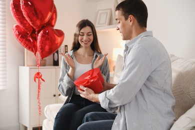 Photo of Lovely man surprising his girlfriend with Valentine's day gift indoors