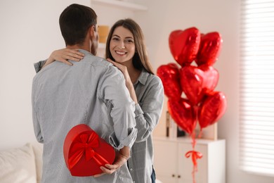 Photo of Lovely man hiding gift box for his beloved woman indoors. Valentine's day celebration