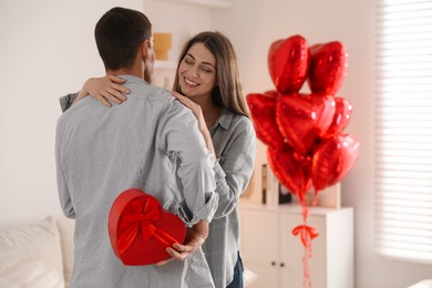 Photo of Lovely man hiding gift box for his beloved woman indoors. Valentine's day celebration