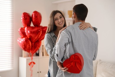 Photo of Lovely man hiding gift box for his beloved woman indoors. Valentine's day celebration