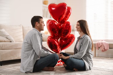 Photo of Lovely couple holding hands near heart shaped balloons indoors. Valentine's day celebration