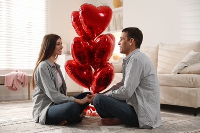 Photo of Lovely couple holding hands near heart shaped balloons indoors. Valentine's day celebration