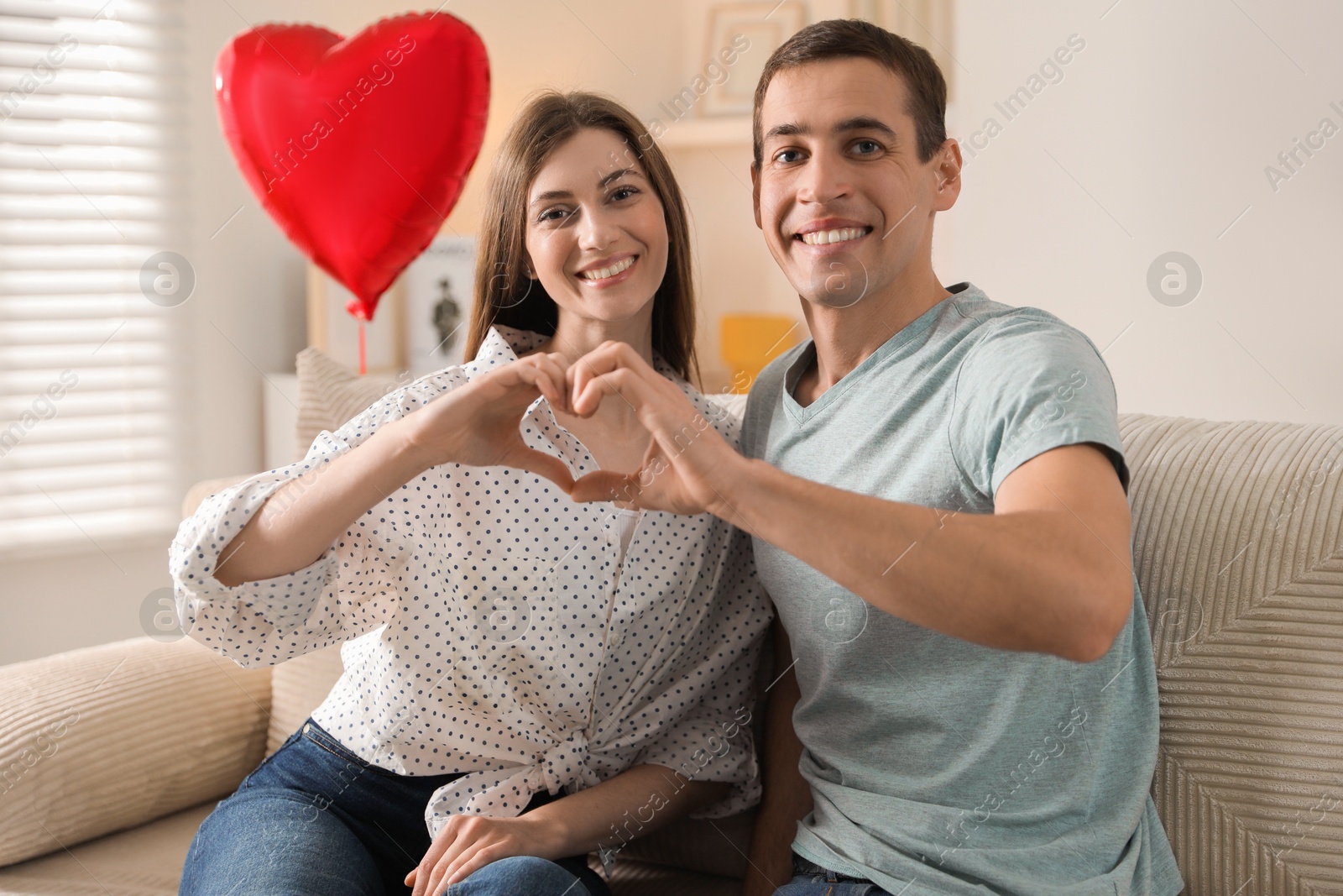 Photo of Lovely couple making heart with hands indoors. Valentine's day celebration