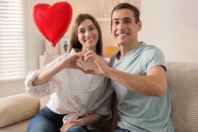 Photo of Lovely couple making heart with hands indoors. Valentine's day celebration