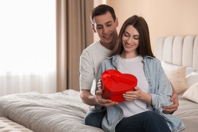 Photo of Lovely couple with gift box indoors, space for text Valentine's day celebration