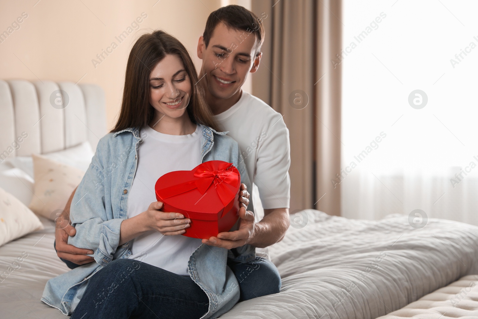 Photo of Lovely couple with gift box indoors, space for text Valentine's day celebration