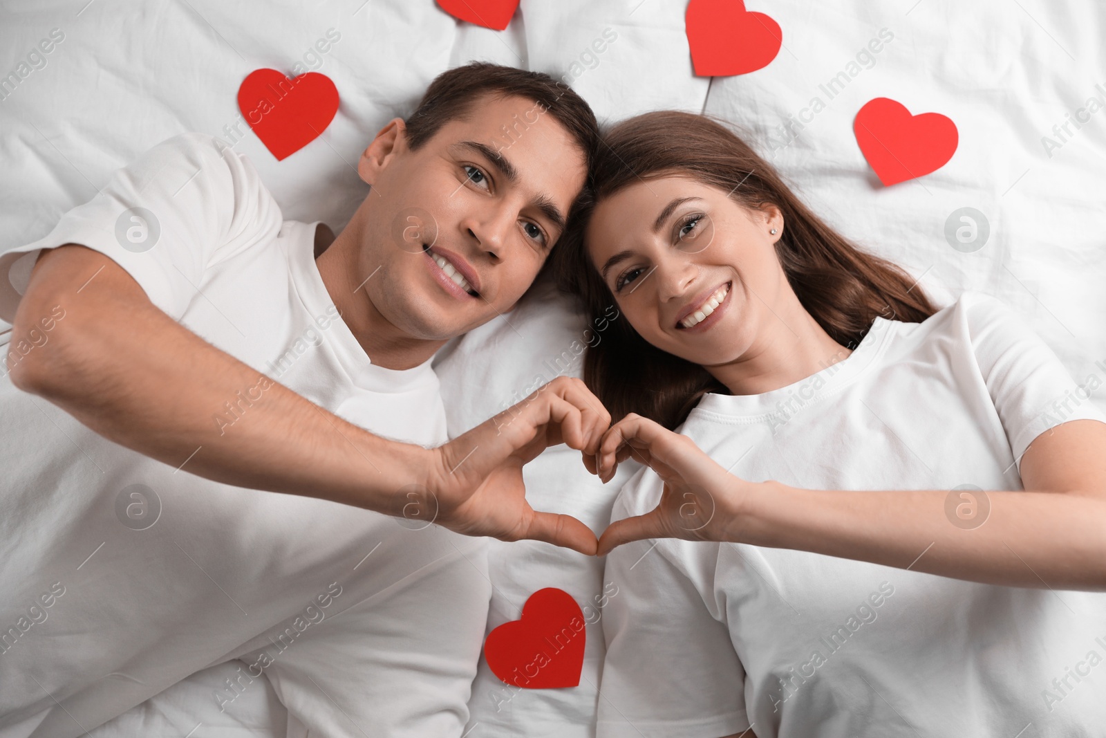 Photo of Lovely couple making heart with hands on bed, top view. Valentine's day celebration