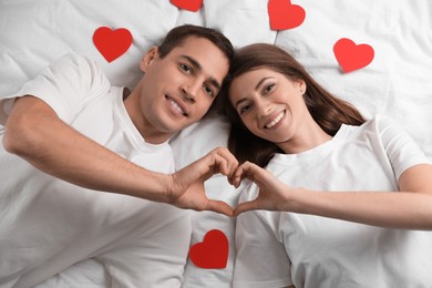 Photo of Lovely couple making heart with hands on bed, top view. Valentine's day celebration