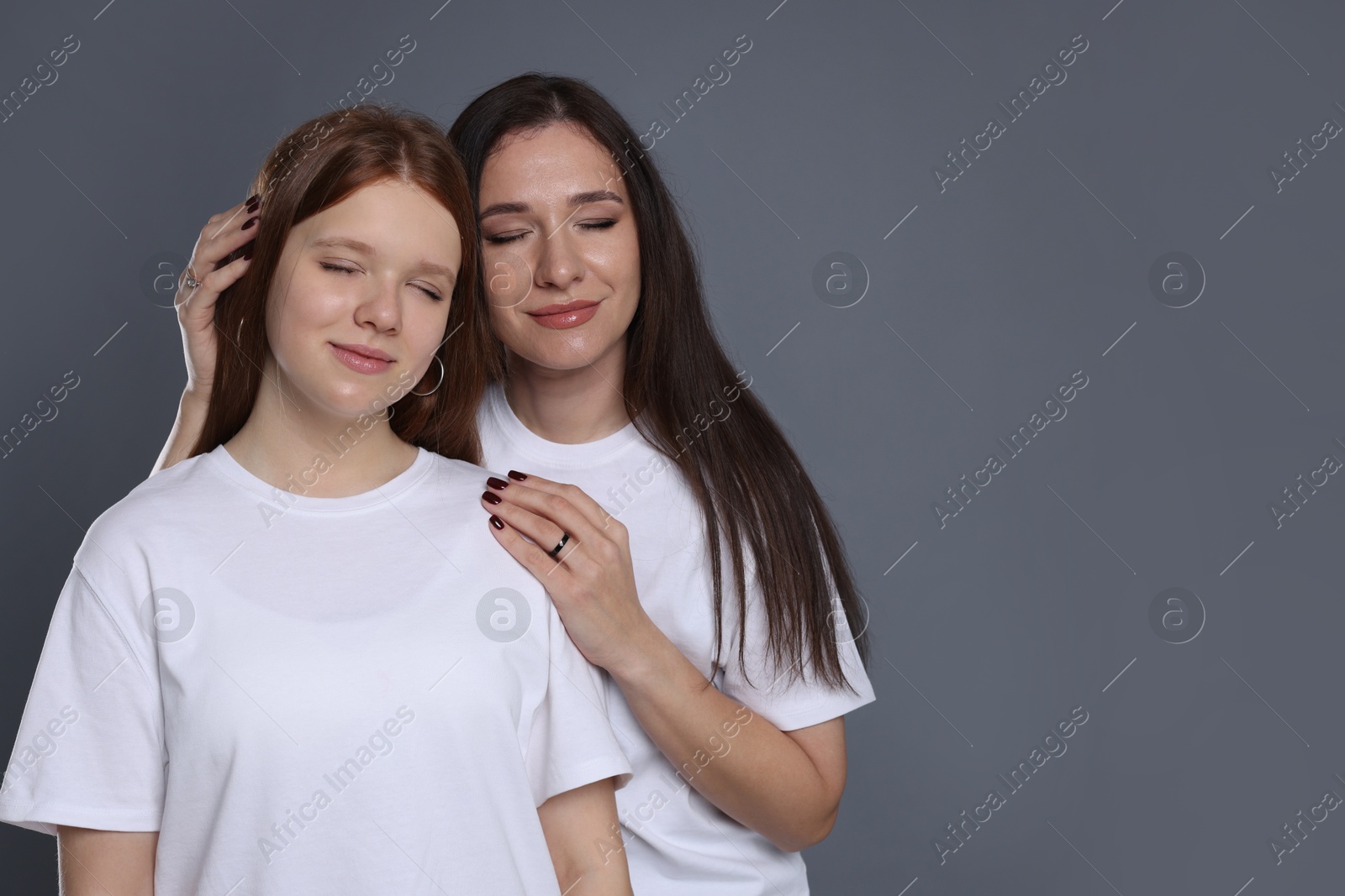 Photo of Family portrait of beautiful mother with teenage daughter on grey background, space for text